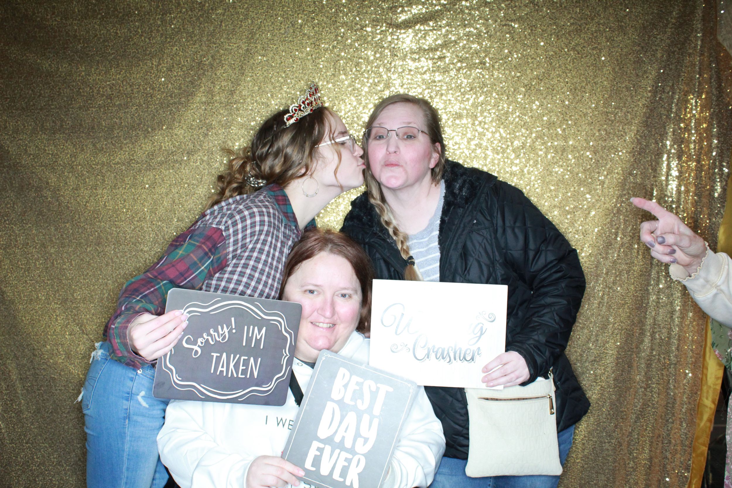 Three people pose with signs against a sparkly gold backdrop at a photo booth party.