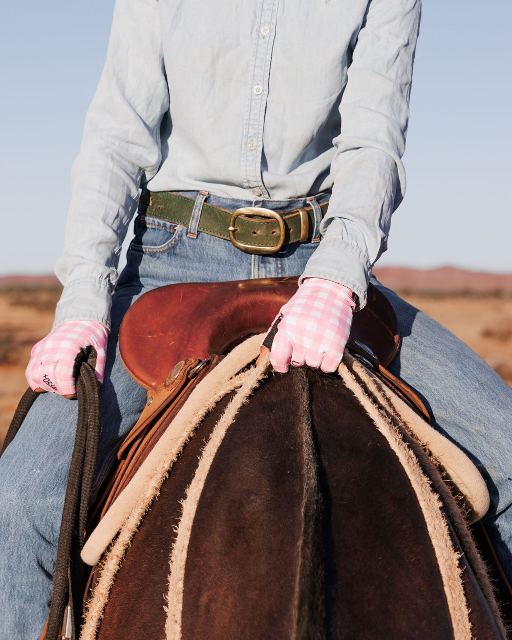 Close-up of western rider's belt and saddle details against desert backdrop.