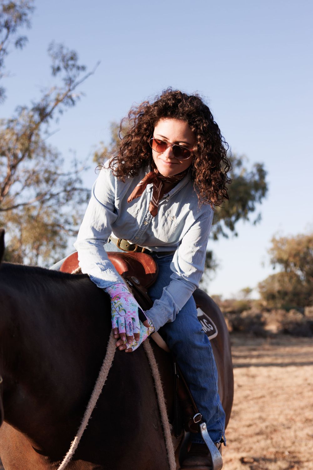 Rider in white shirt and jeans sitting astride a dark horse in an outdoor setting.