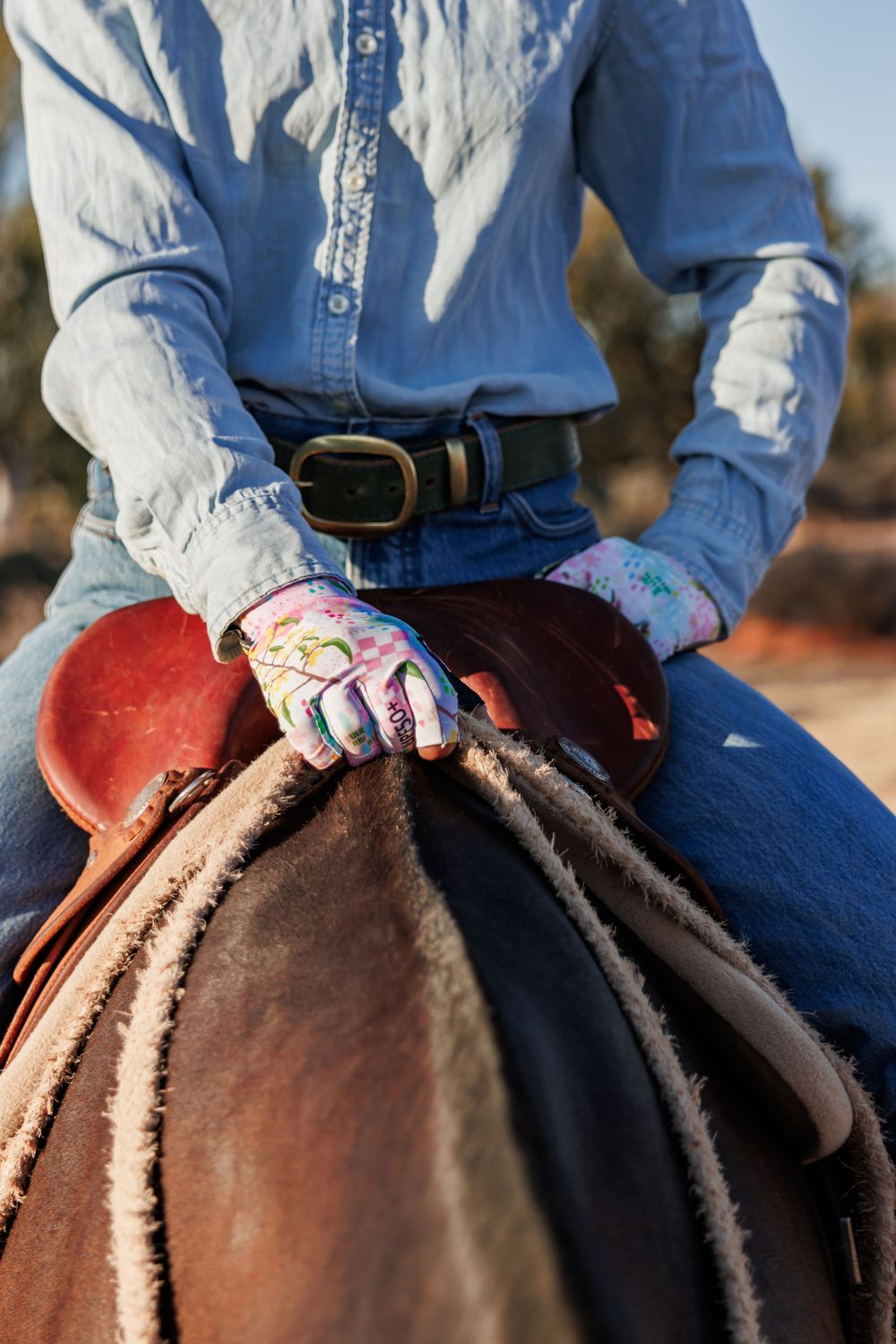 Close-up of patterned riding gloves gripping a western saddle horn.