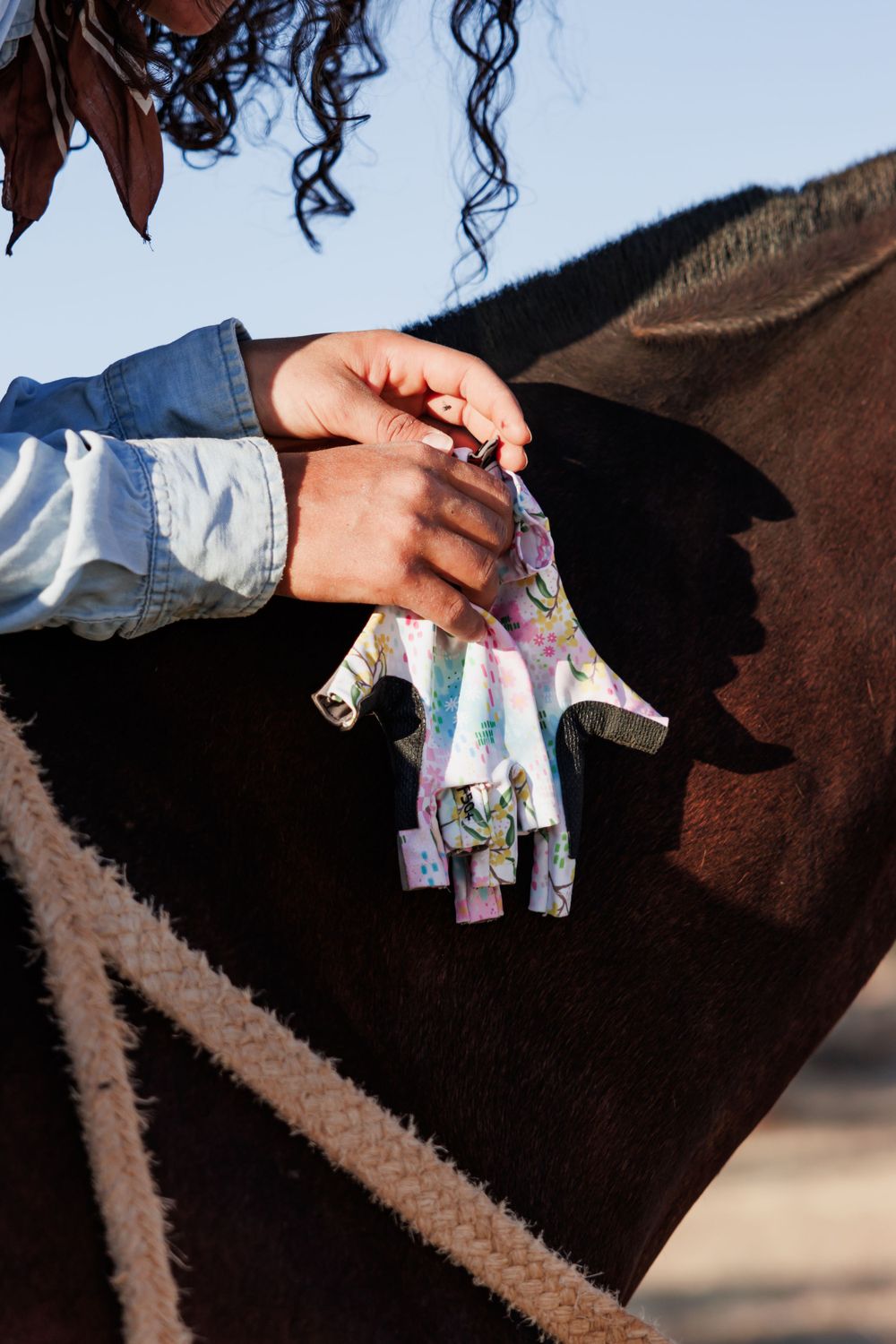 Close-up of hands removing floral print riding gloves while sitting on horseback.