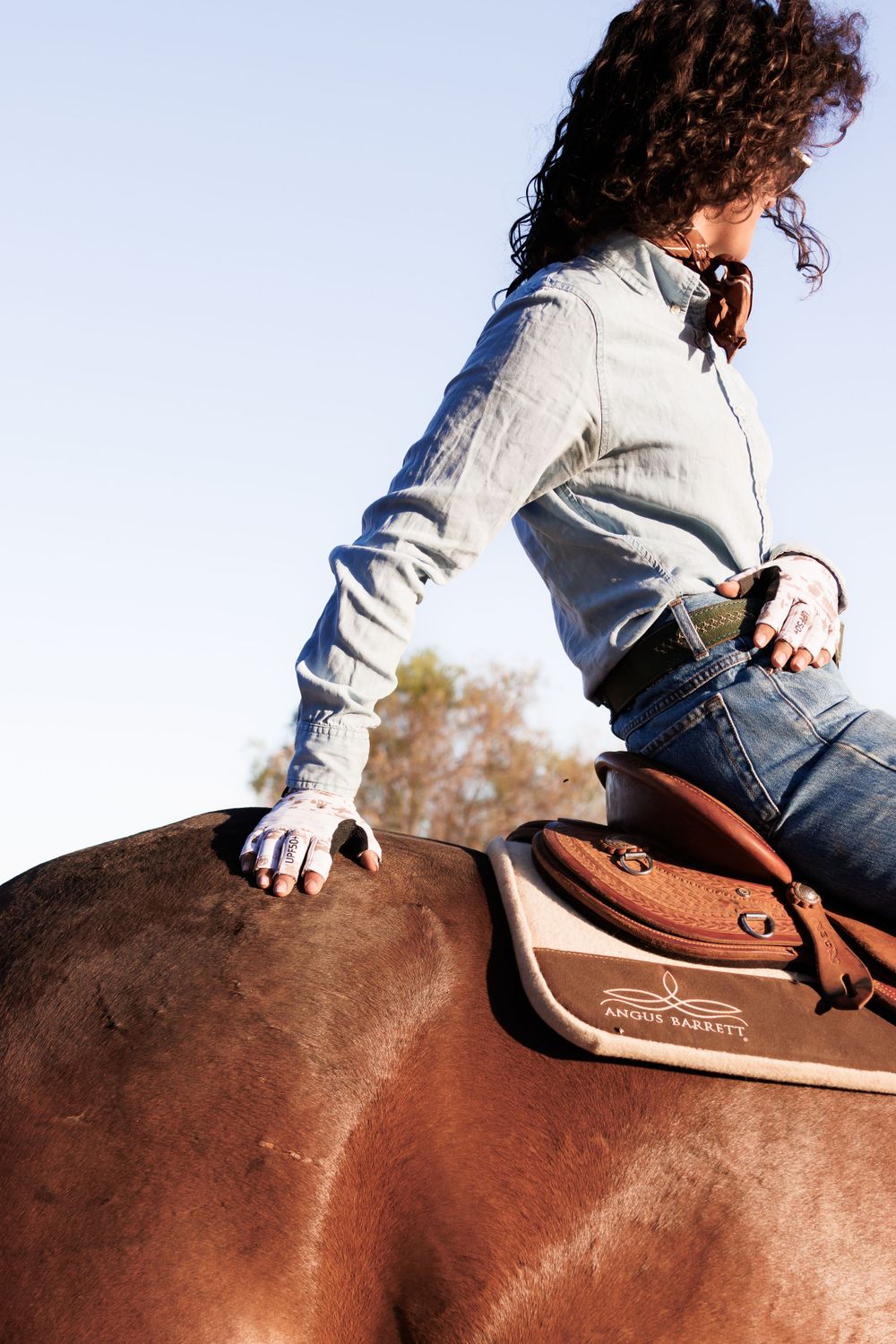 Side view of rider mounted on brown horse with leather western saddle.