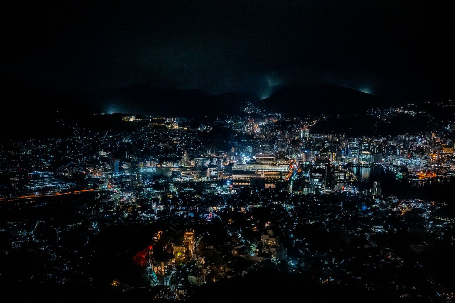 Aerial nighttime cityscape showing illuminated buildings and streets under dark sky.