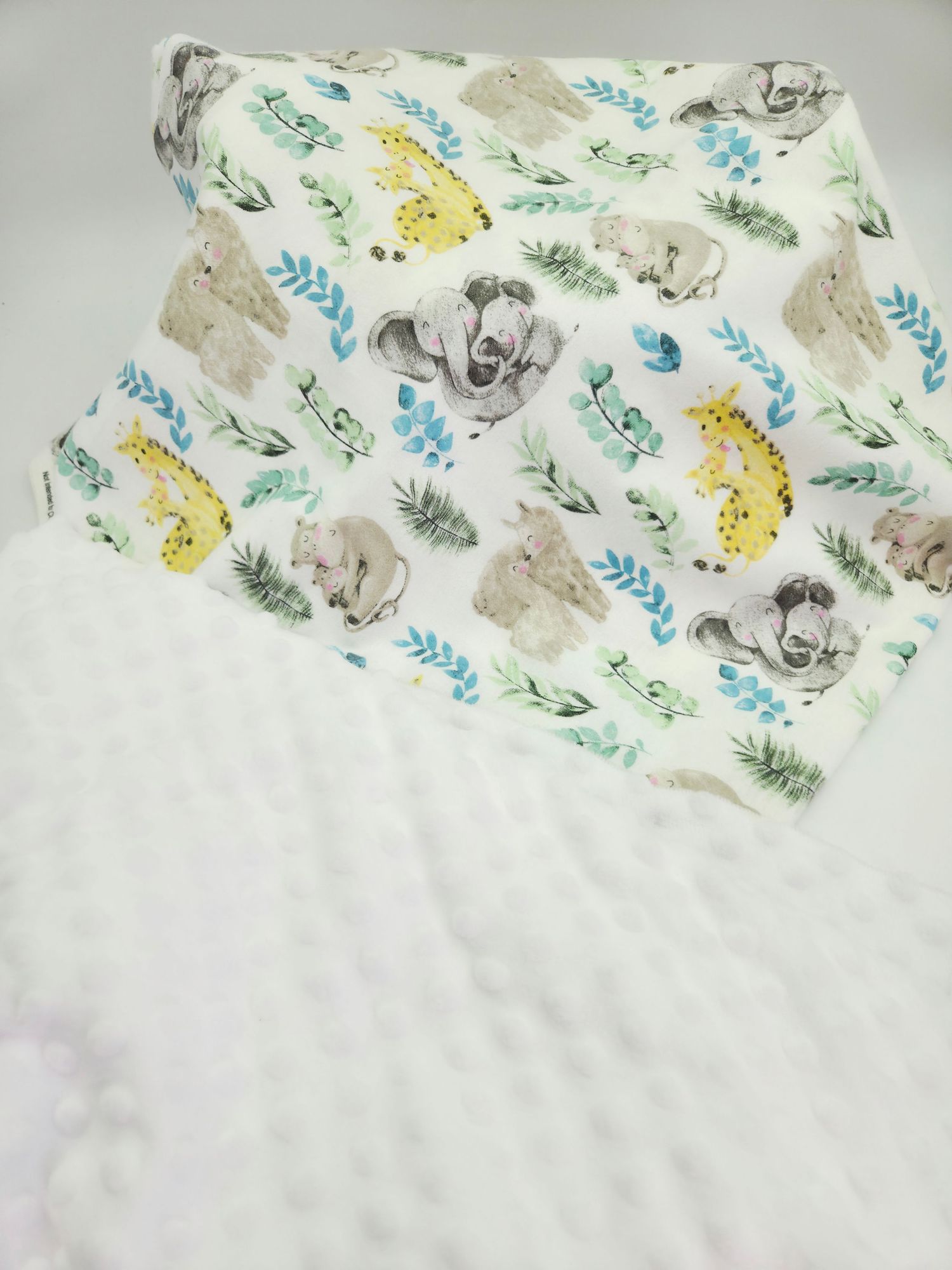 White baby blanket featuring adorable safari animals and foliage print in soft pastel colors.