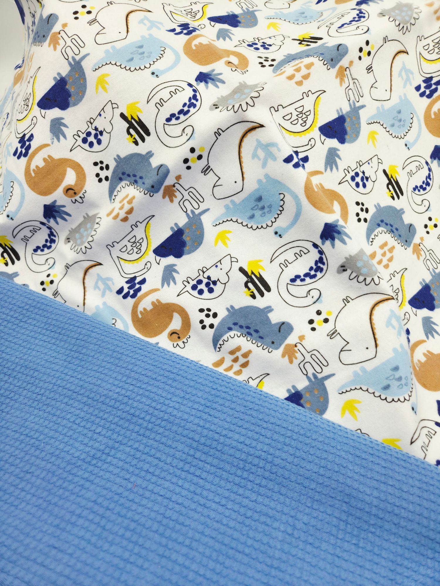 A seamless pattern of cute dinosaurs and moons in blue, brown and yellow tones on white fabric with matching blue textile.