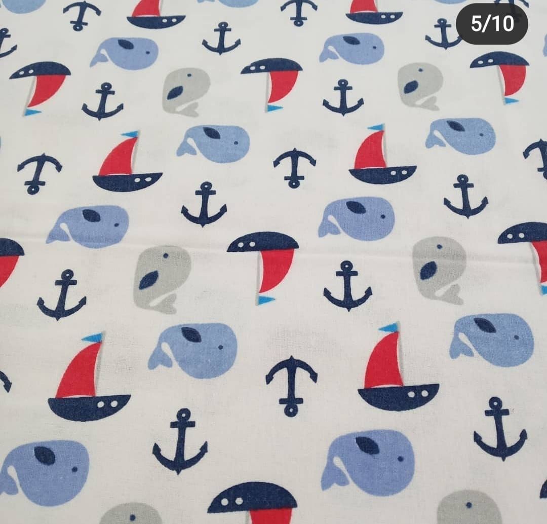 Nautical fabric print featuring blue whales, red sailboats, and navy anchors on a white background.