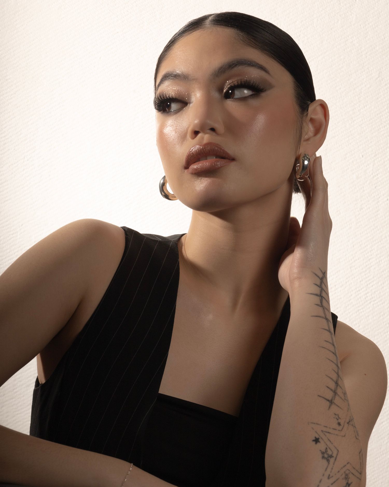 Dramatic studio portrait featuring sleek hair, bold makeup, and minimalist black attire.