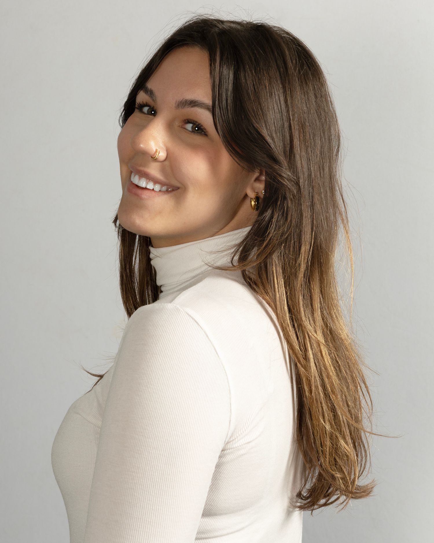 Professional headshot in white turtleneck with natural lighting and warm smile.