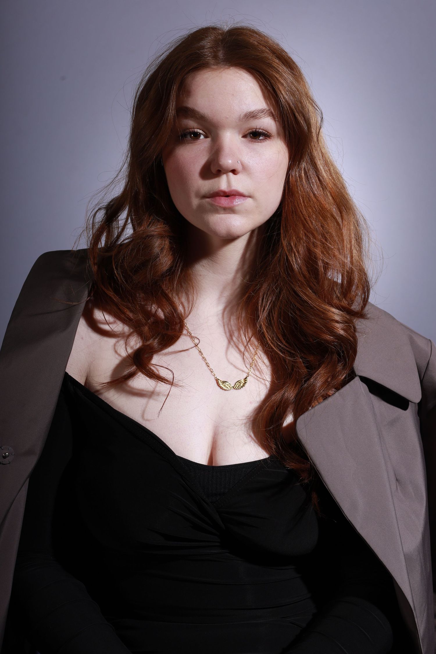 Studio portrait featuring natural makeup and black outfit with beige overcoat.