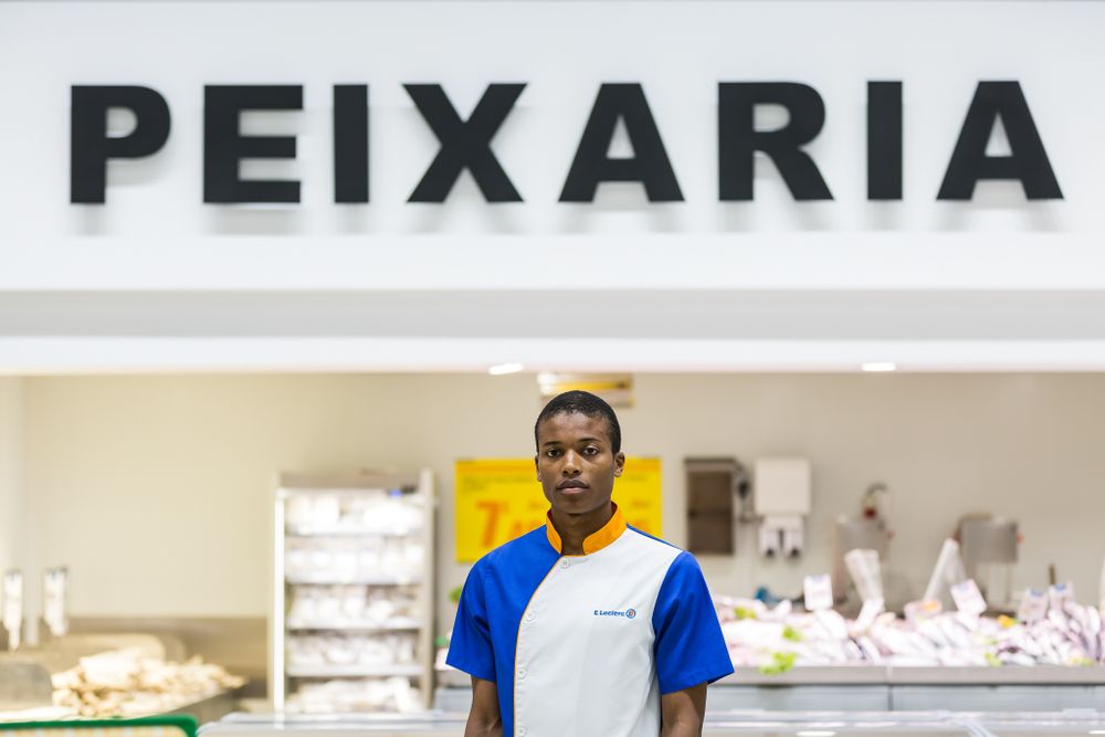 Staff member stands in front of a peixaria (fish market) sign at a seafood counter in Brazil.