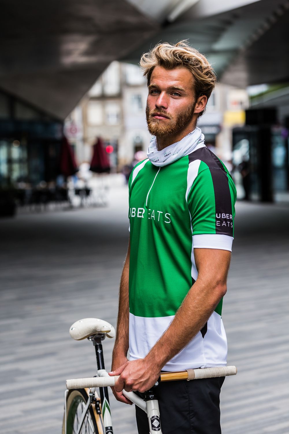 Cyclist wearing green and white athletic jersey standing with classic bicycle in urban setting.