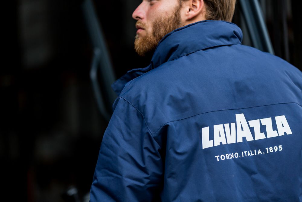 Person wearing a blue Lavazza branded jacket with text Torino Italia 1895.