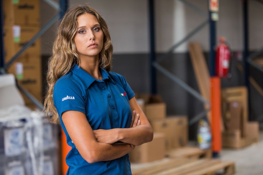 A professional worker in a blue uniform stands confidently in a warehouse storage facility.