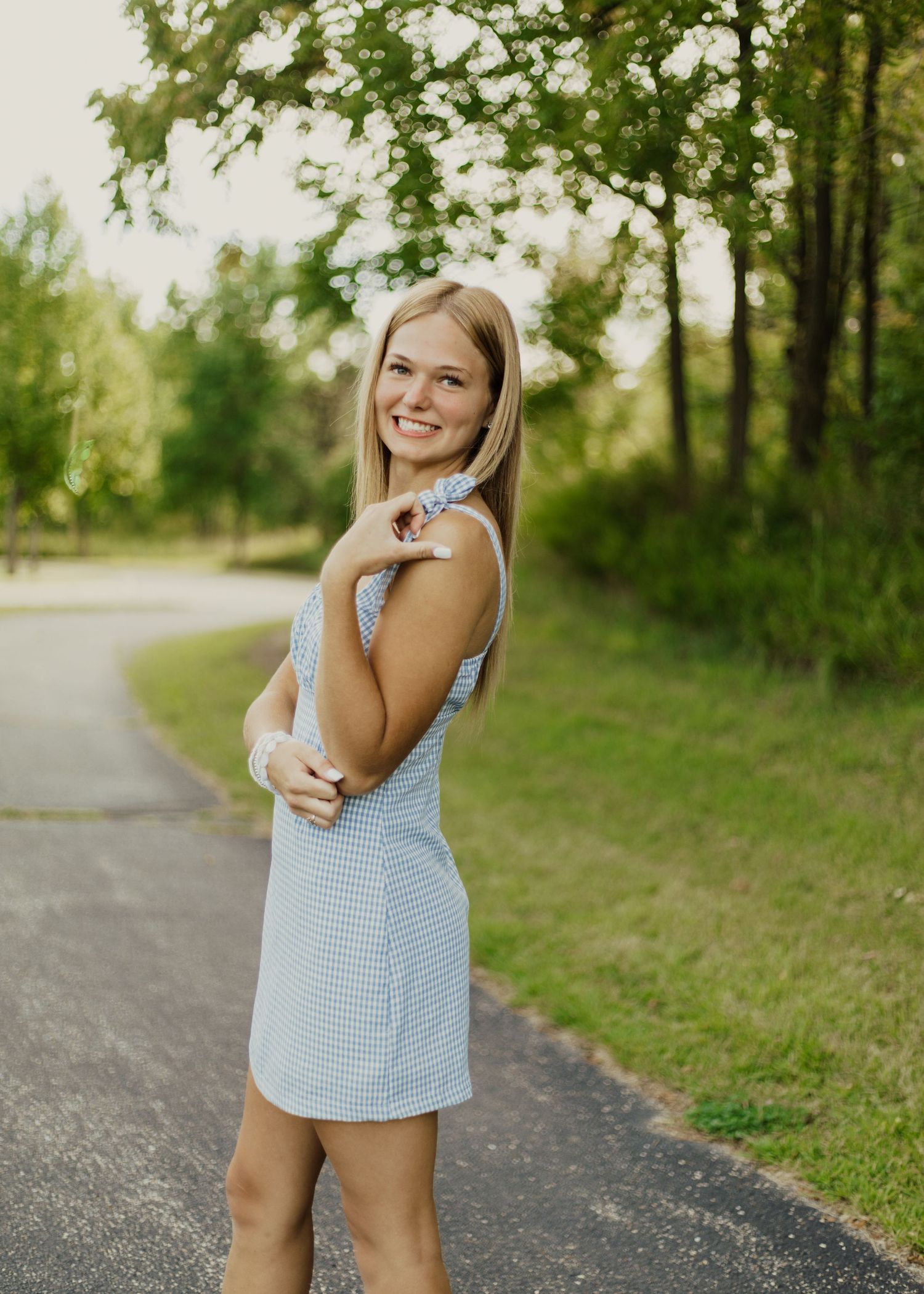 A light blue and white gingham dress being worn on a scenic path surrounded by green trees on a bright summer day.