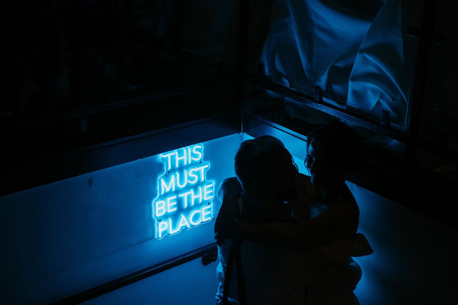 Silhouette of a person against a glowing blue neon sign that reads 'This must be the place' inside Twist Gallery located in Toronto Canada