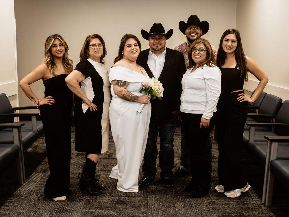 A wedding party poses together in formal attire with the couple in the center of the group.