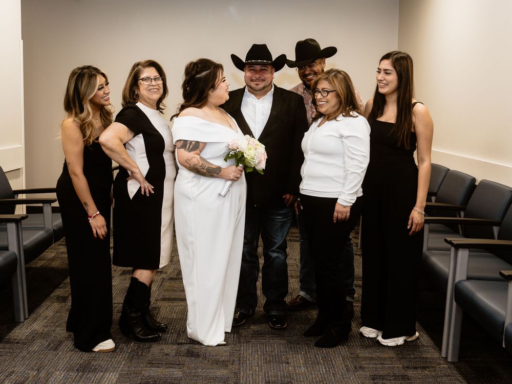A formal wedding party in black and white attire stands together in a carpeted indoor venue.