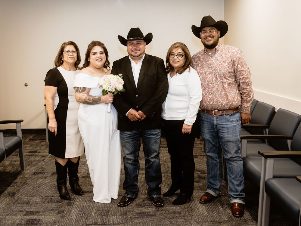 A group of people in western attire pose together in a casual indoor setting with a sofa visible in the background.