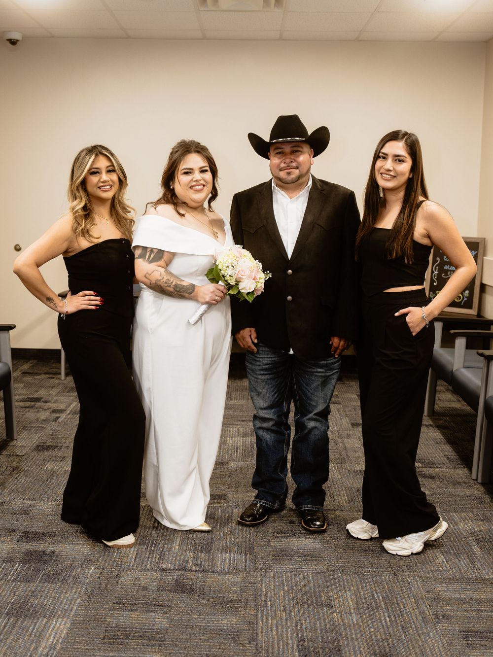 Wedding party poses together in elegant attire including black dresses, a white gown, and western cowboy style.