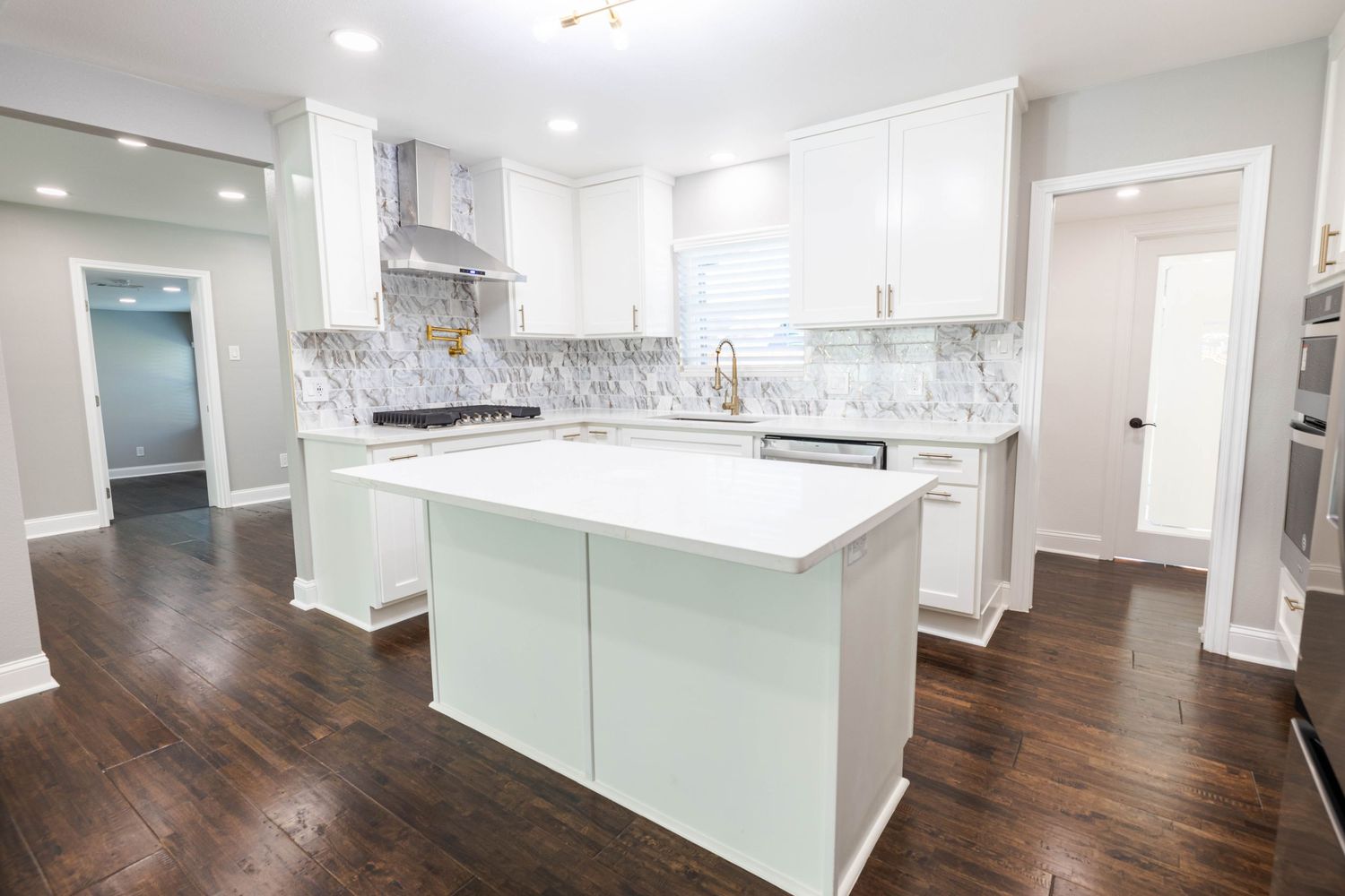 Modern white kitchen interior with dark hardwood floors and bright recessed lighting.