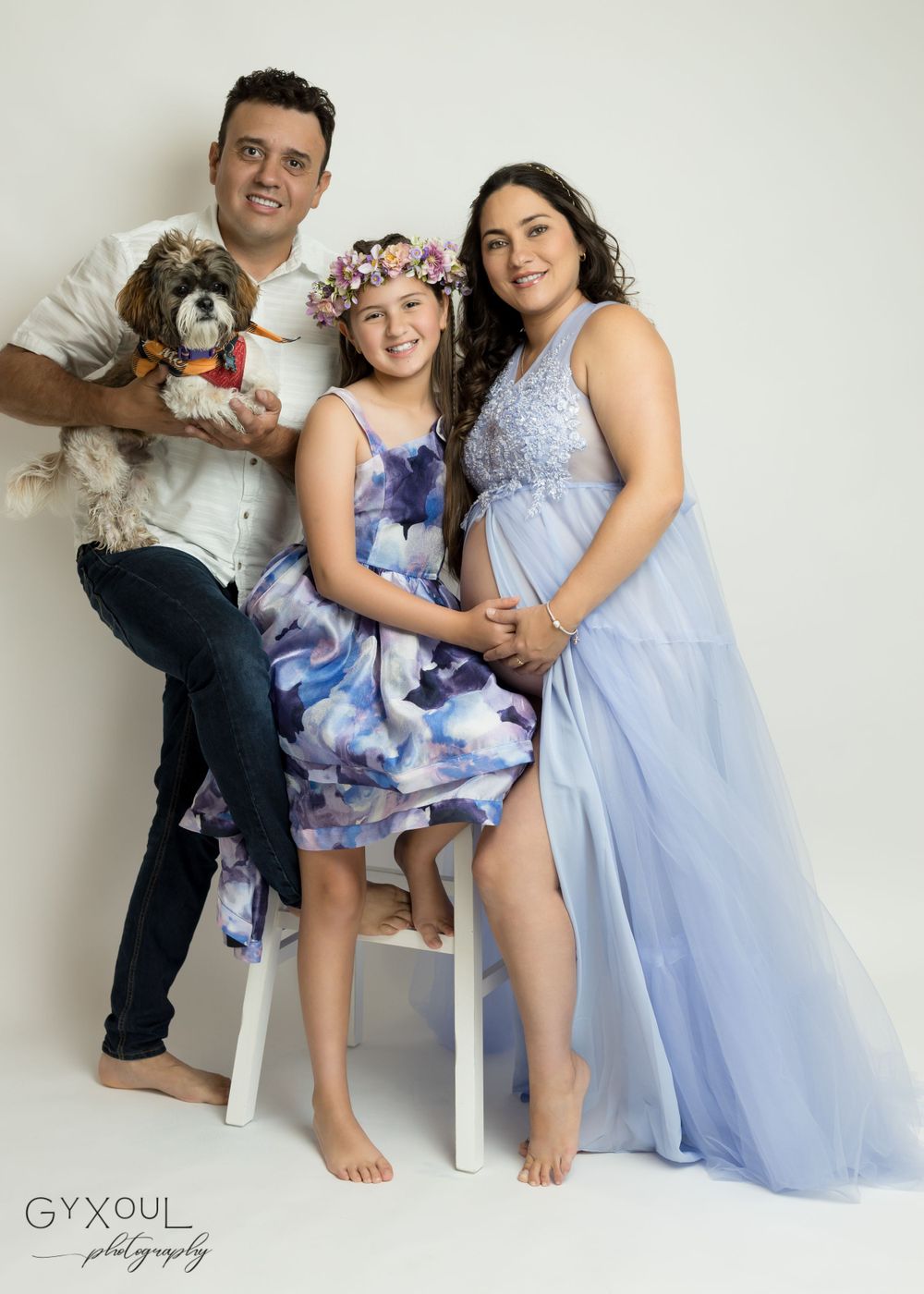 A family poses together in coordinating blue outfits with their small fluffy dog for a studio portrait.