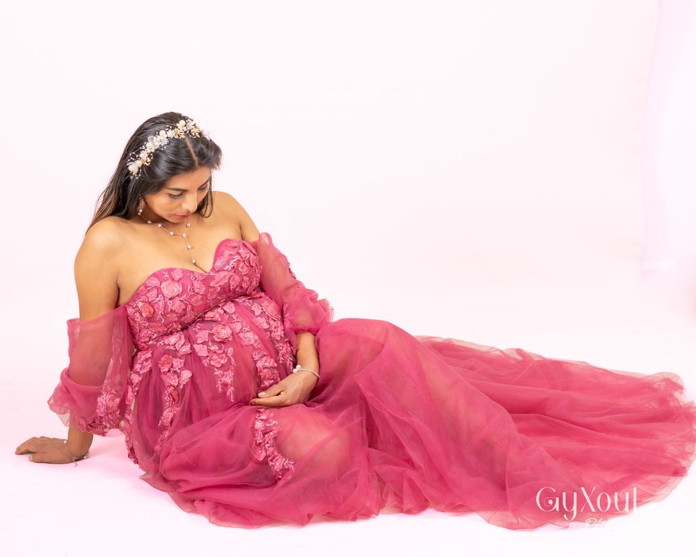 Elegant maternity portrait in flowing pink tulle gown against light backdrop.
