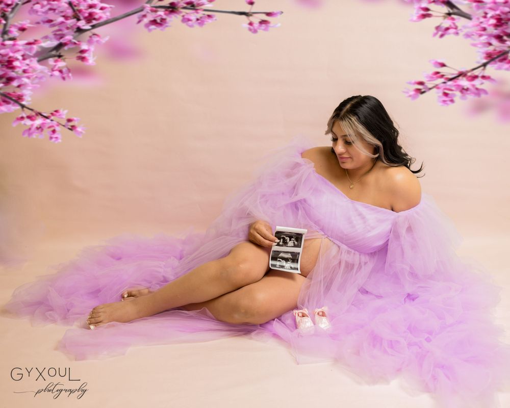 Dreamy maternity photo with cherry blossoms and pink tulle dress holding ultrasound image.