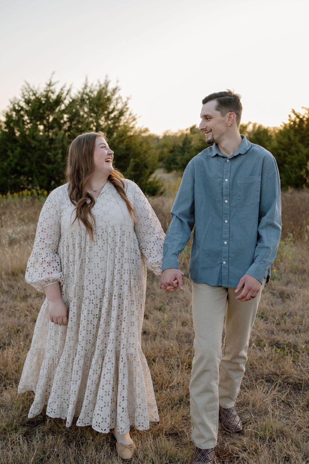 Couple in casual attire share a joyful moment in a golden field at sunset.