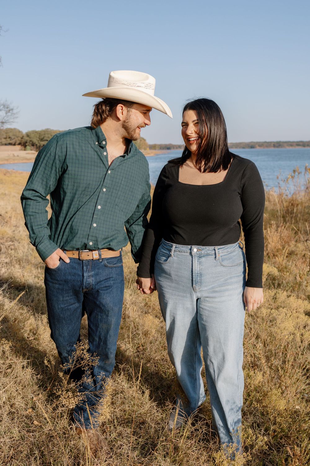 A country western couple in casual attire standing together by a lake.