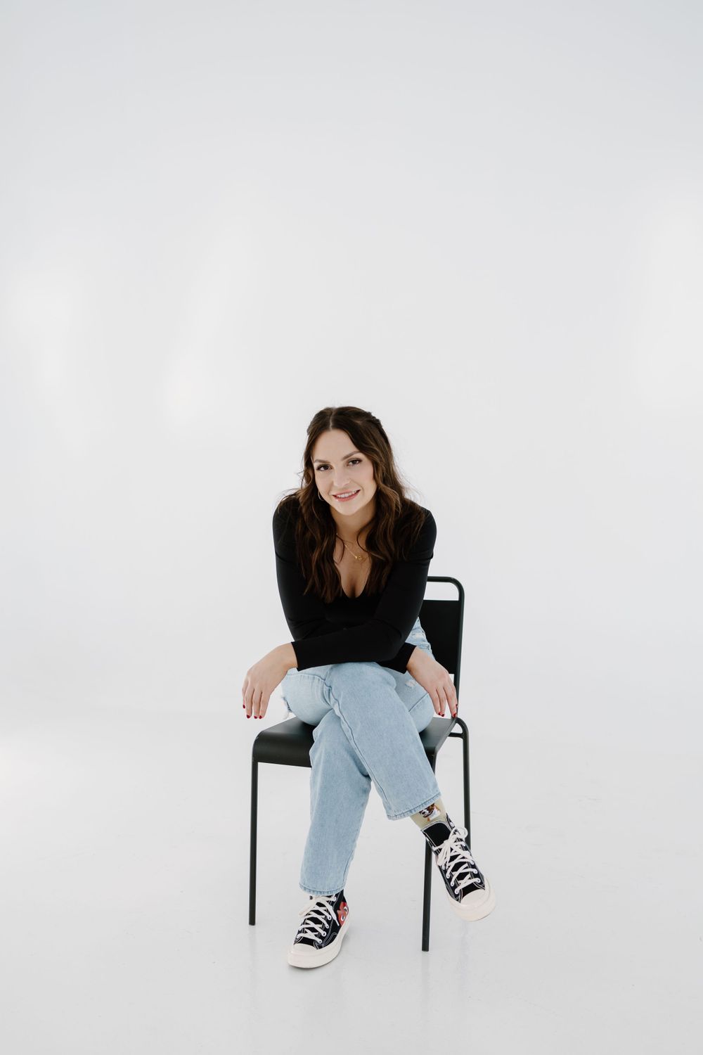 Casual portrait of woman in black sweater and jeans sitting on chair in studio setting.