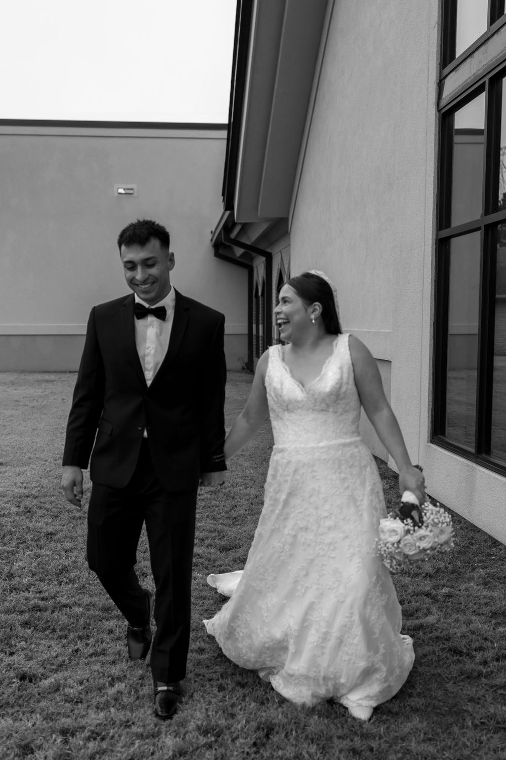 Black and white candid shot of a walking newlywed couple outside a modern building.