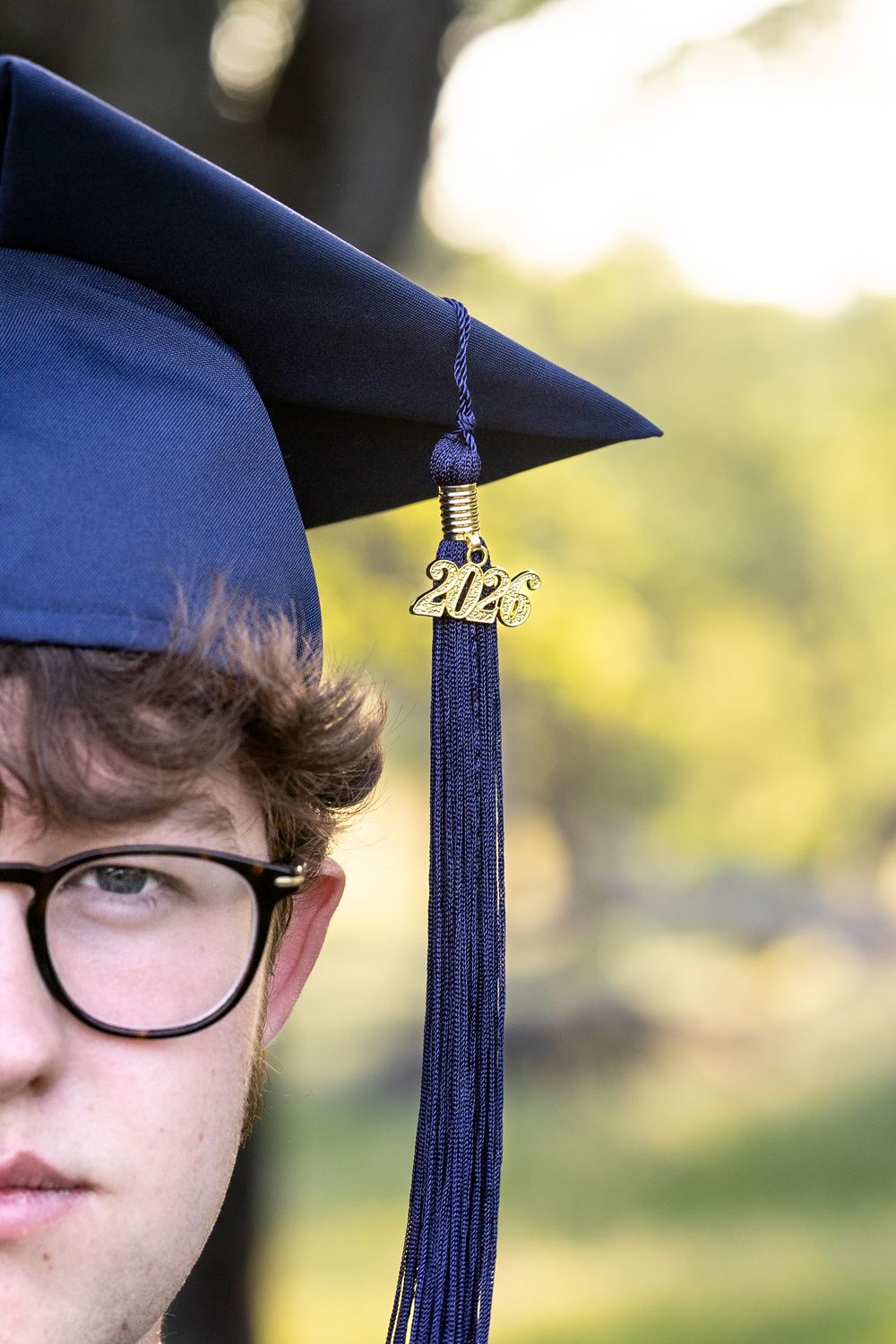 Close-up view of a graduation cap tassel against a blurred green outdoor background.