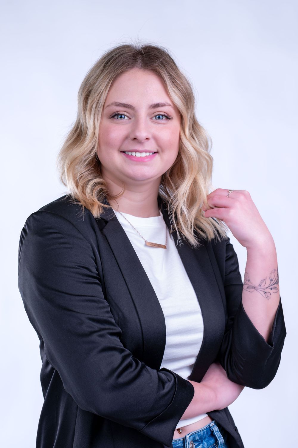 Professional headshot with wavy blonde hair wearing black blazer and white top against light backdrop.