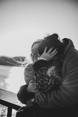 A tender embrace captured in black and white photography beside a sunlit backdrop.