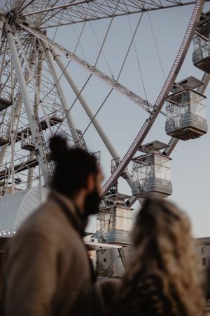 A silhouetted couple gazing up at a large ferris wheel against a bright sky.
