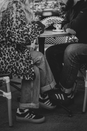Black and white photo of people sitting at a cafe, showing leopard print coat and casual sneakers.