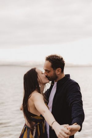 Romantic sunset photoshoot by the water showing tender embraces and kisses.