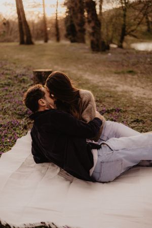 Couple sharing intimate moments while lying on a blanket surrounded by spring flowers in a park.