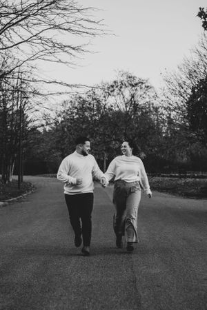 Photo en noir et blanc d'un couple dans un parc. Il court ensemble main dans la main
