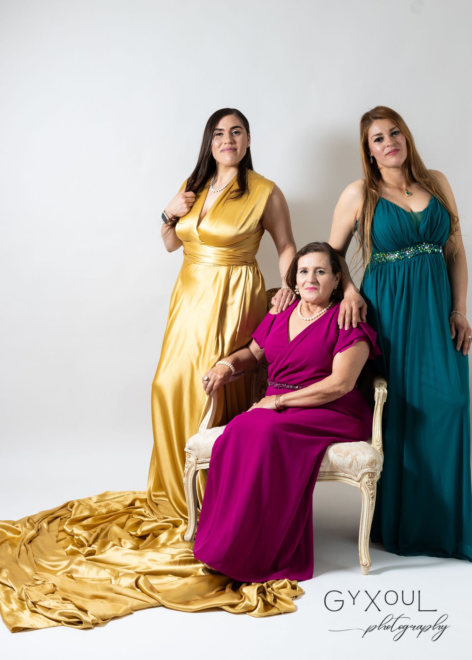 Three women in formal gowns - yellow, magenta and teal - pose elegantly in a studio setting.