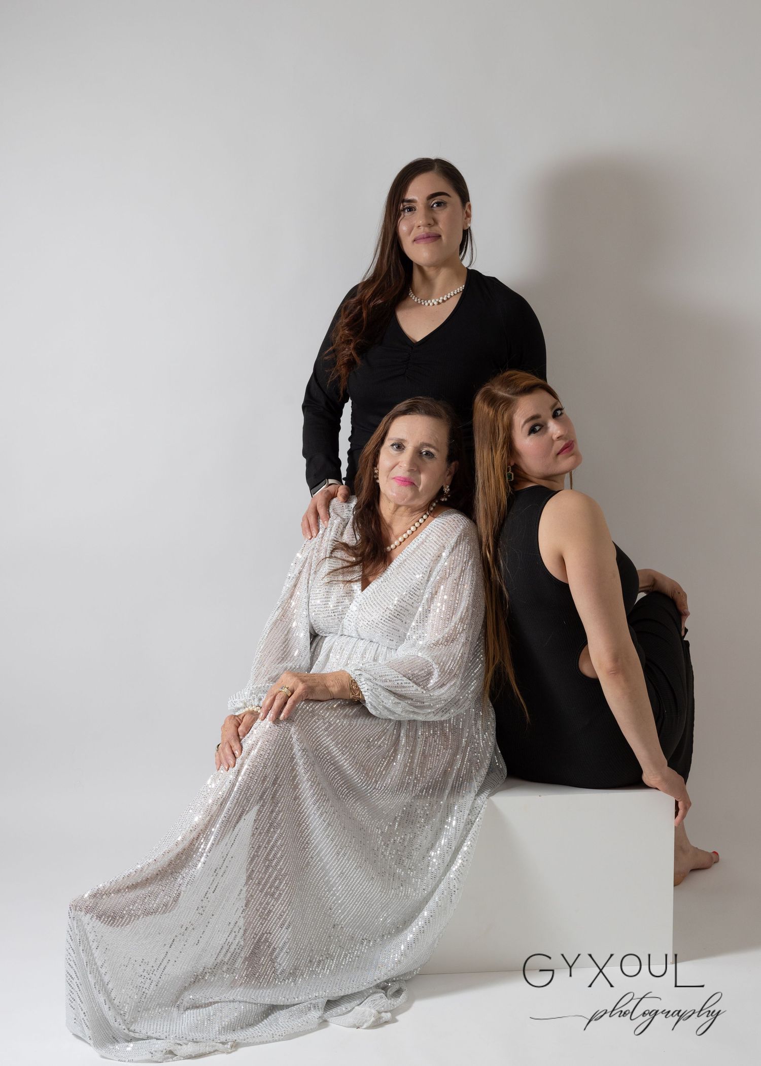 Three women pose artistically in black and white outfits against a plain studio background.