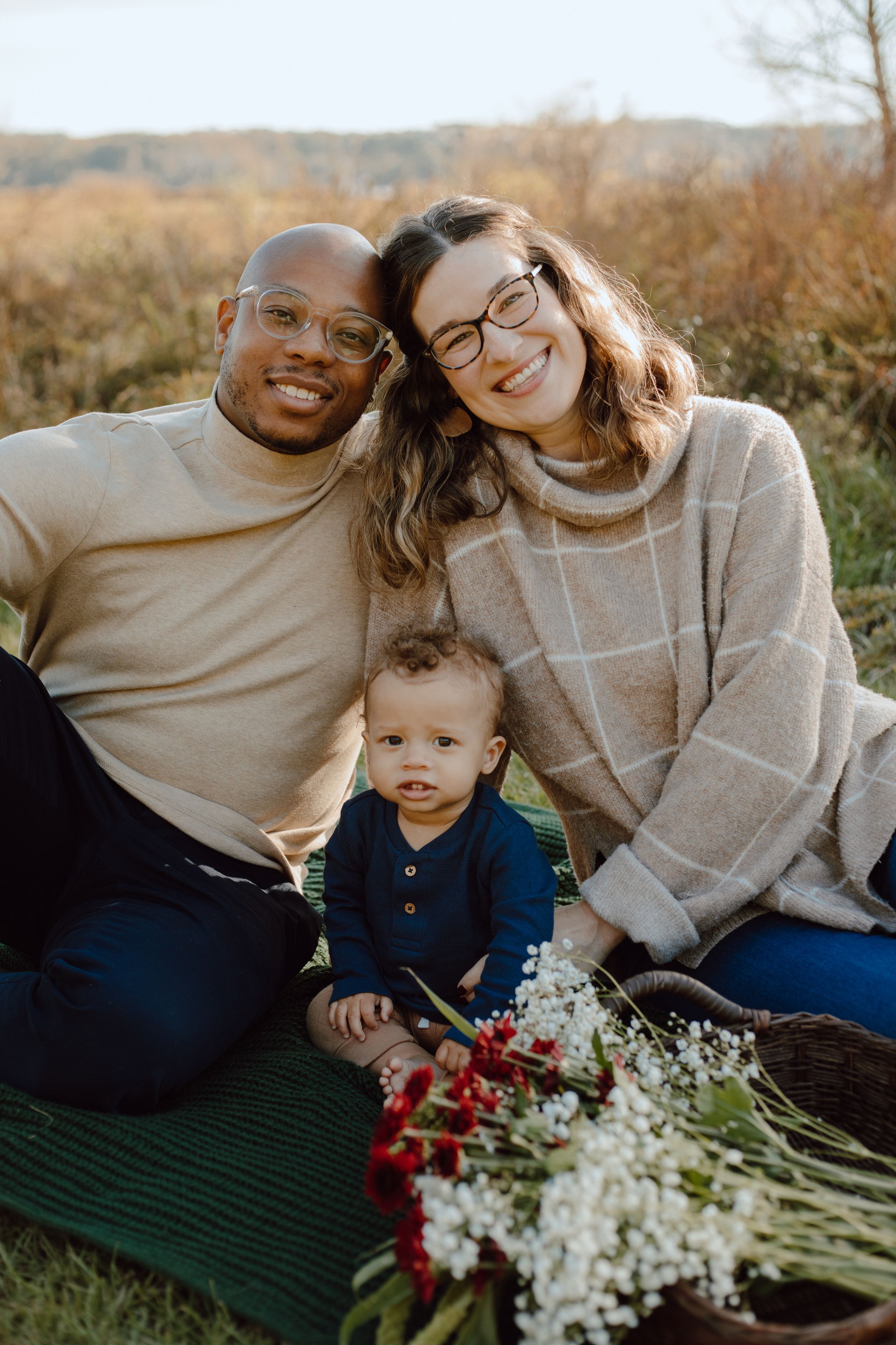 Family sitting on blanket outdoors with flowers during autumn photoshoot.