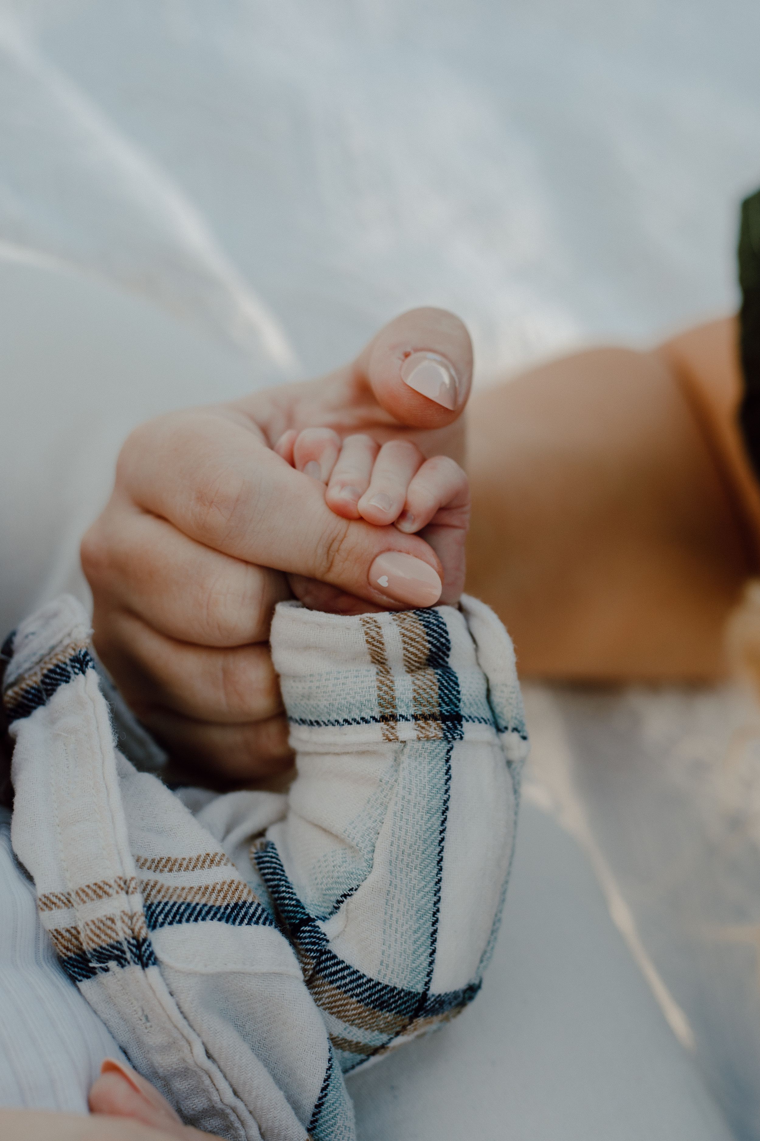 Close-up of tiny baby fingers being held against a plaid fabric background.