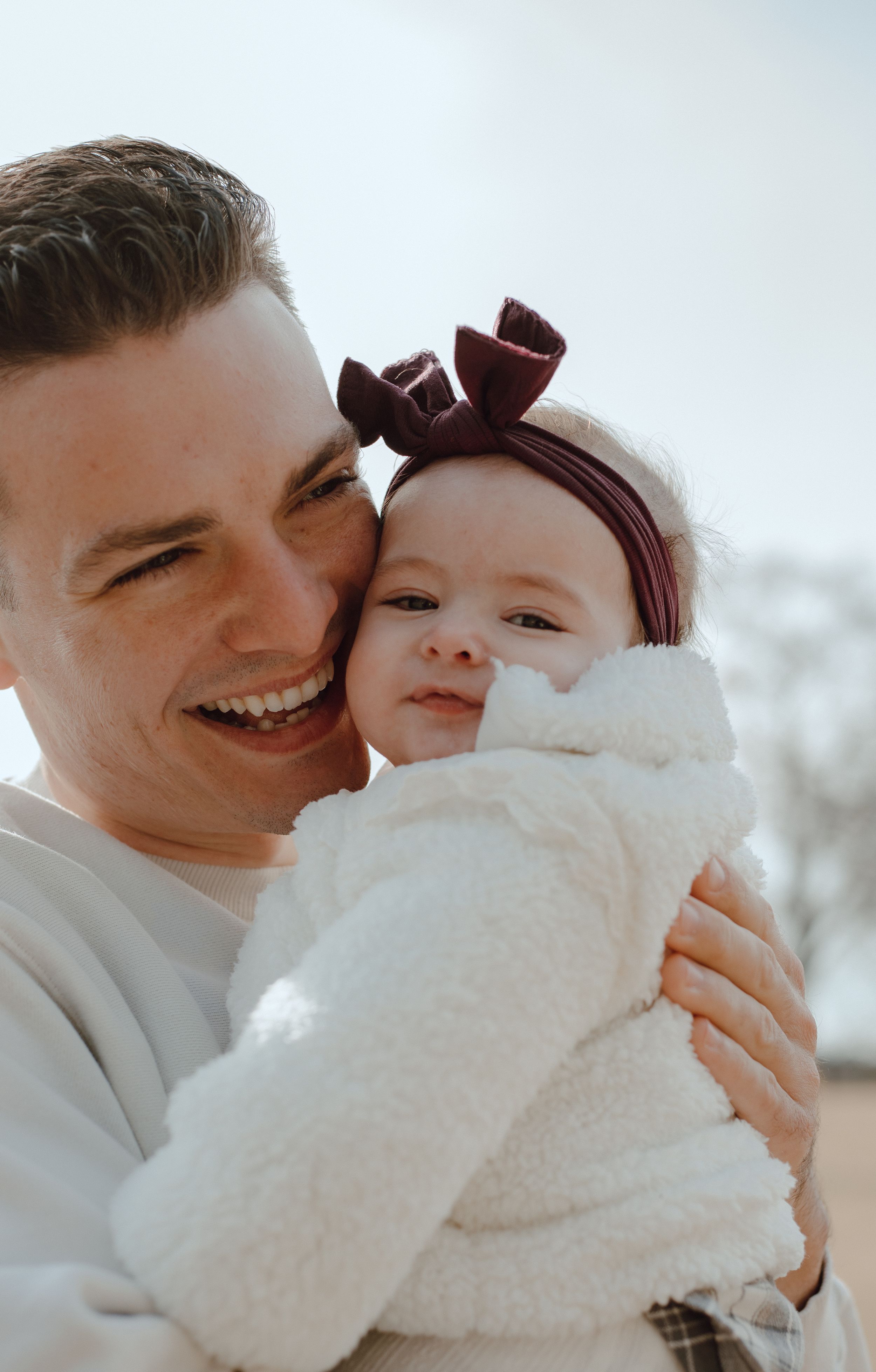 A joyful parent and baby share a candid laughing moment together while the baby wears a burgundy headband.