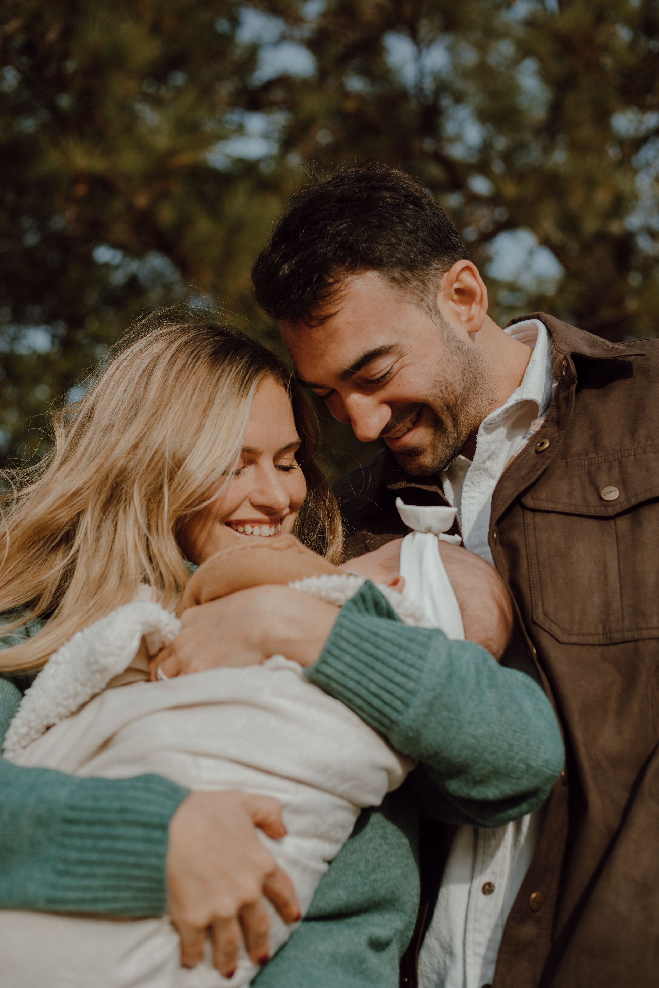 A couple shares an intimate moment outdoors, embracing and laughing together in warm autumn lighting.