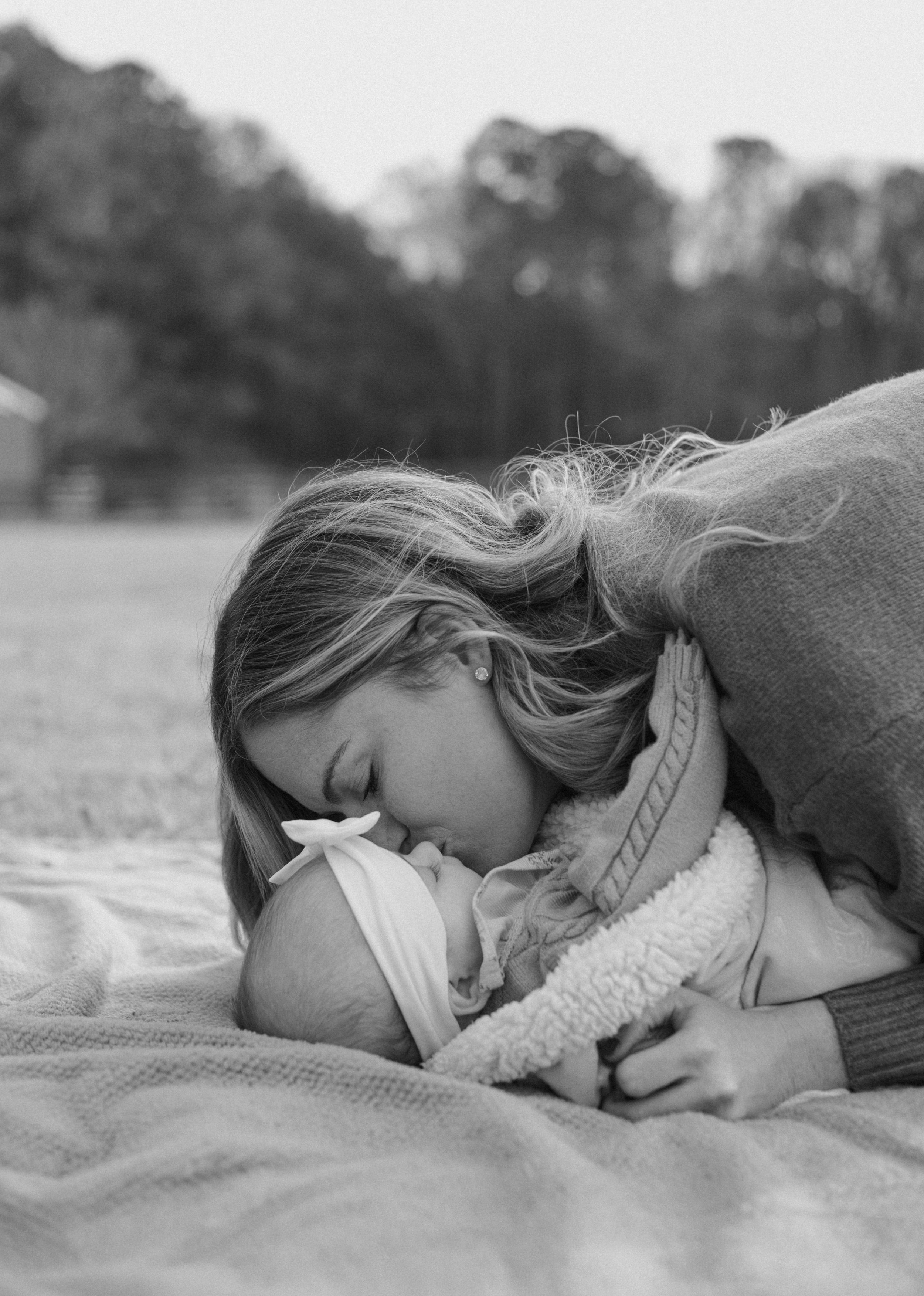 A tender black and white photograph of a parent and child sharing an intimate moment while lying on a blanket outdoors.