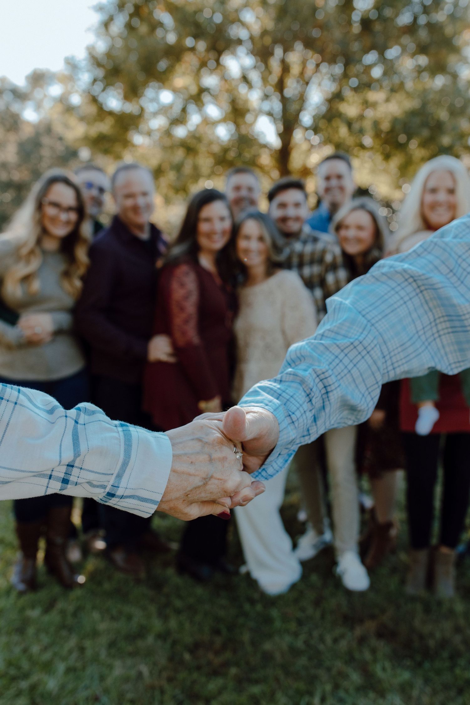 Close-up of hands clasped together with a group of people standing in the background outdoors.