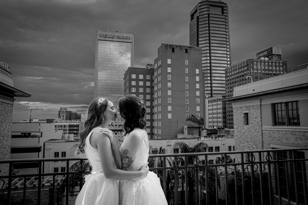 A romantic black and white jacksonville cityscape portrait with a same sex couple in wedding dresses on a rooftop.
