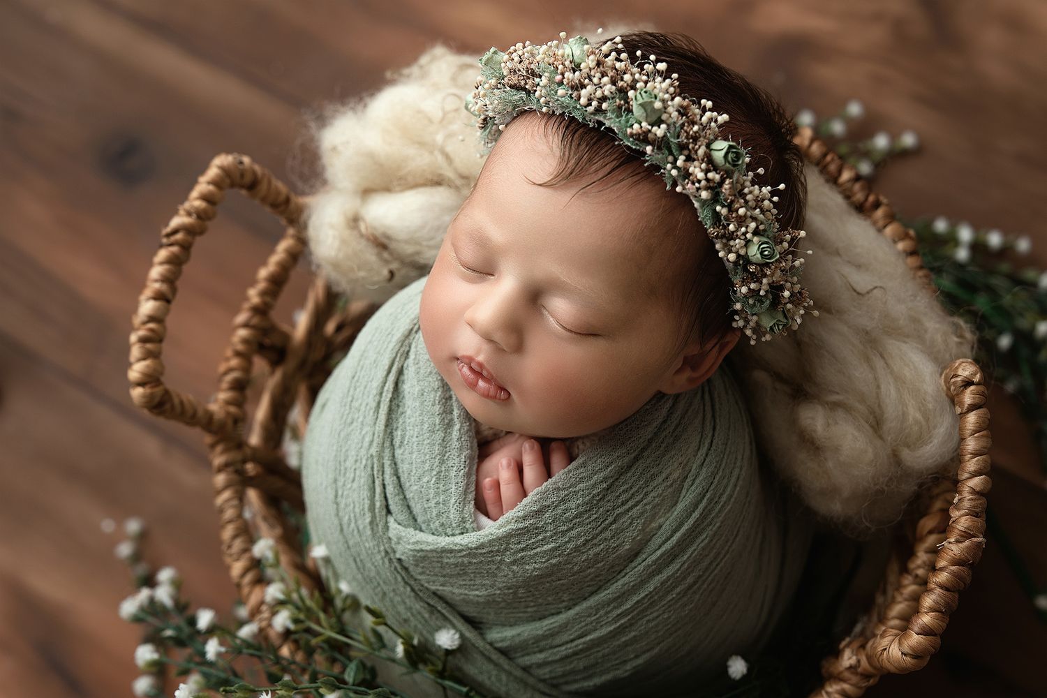 Sleeping newborn wearing delicate crystal crown wrapped in sage green swaddle.