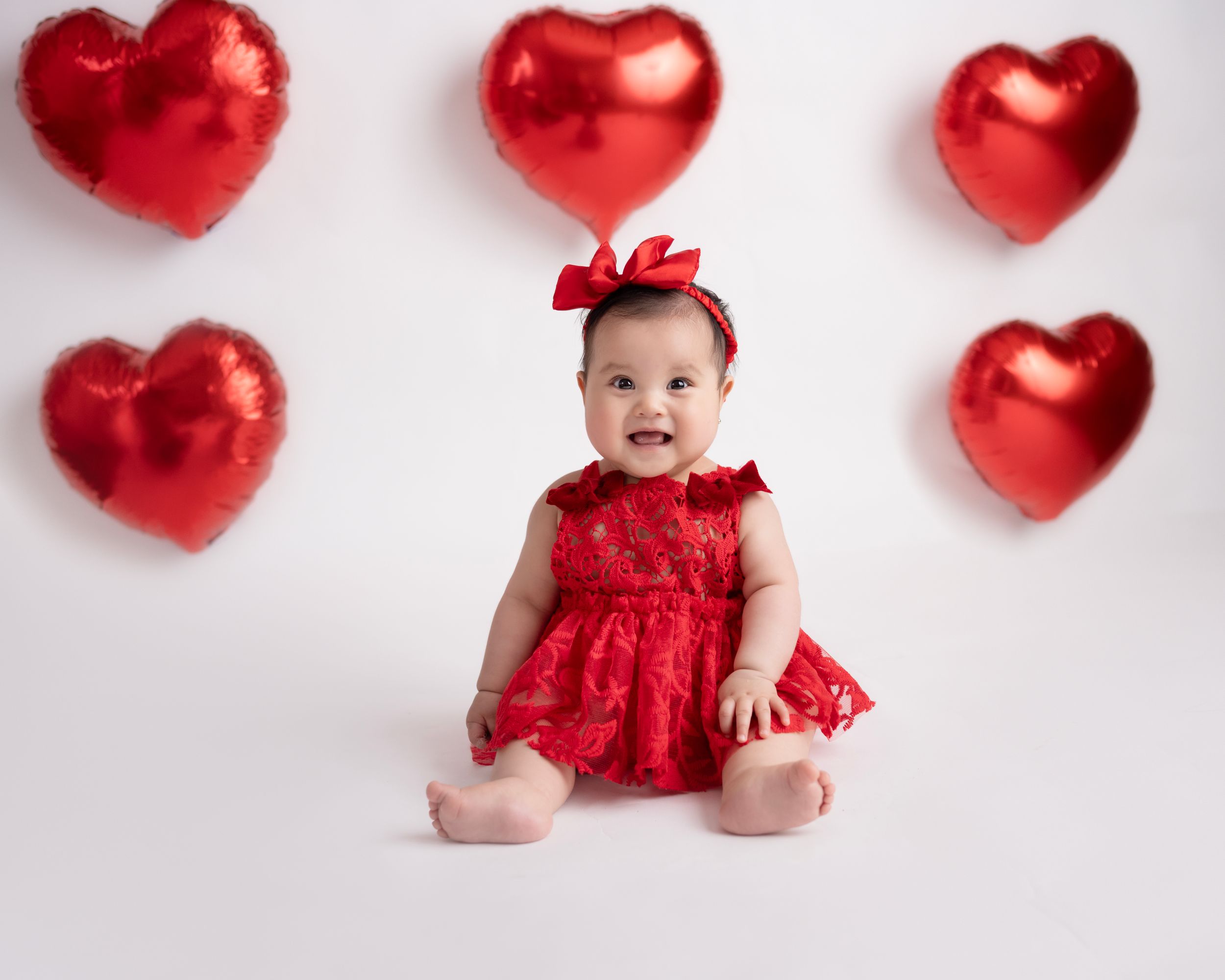 Professional baby photo with metallic red hearts scattered on white background.